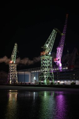 Lux Helsinki ışık festivali sırasında gece Helsinki Limanı 'nın üzerinde renklerle aydınlatılmış vinçler yükseliyor. Suda parıldayan parlak yansımalar, çarpıcı bir kentsel mirasa dönüşen kentsel sanayi mirasını vurguluyor.