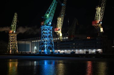 Lux Helsinki ışık festivali sırasında gece Helsinki Limanı 'nın üzerinde renklerle aydınlatılmış vinçler yükseliyor. Suda parıldayan parlak yansımalar, çarpıcı bir kentsel mirasa dönüşen kentsel sanayi mirasını vurguluyor.