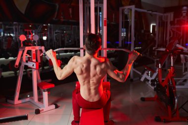Yakışıklı fitness adamı, makineye dönmek için ağırlık egzersizi yapıyor. Kırmızı arka plan ışığı