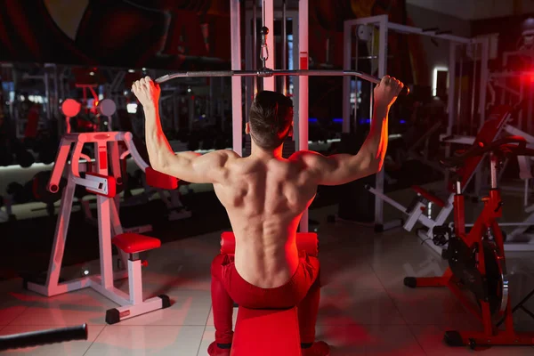 機械に戻るための重い重量の練習をするハンサムな適性の人 赤の背景光 — ストック写真