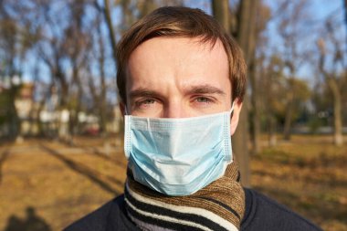 Tıbbi maskeli genç adamın portresi şehir caddesinde duruyor. Dışarıdaki kalabalığın içinde virüsten koruyucu maske takan adam. Coronavirüs salgınından sağIık ve güvenlik kavramı.