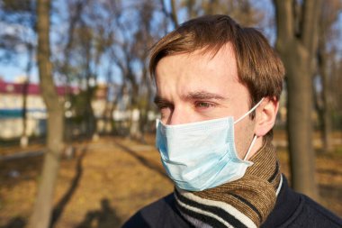 Tıbbi maskeli genç adamın portresi şehir caddesinde duruyor. Dışarıdaki kalabalığın içinde virüsten koruyucu maske takan adam. Coronavirüs salgınından sağIık ve güvenlik kavramı.