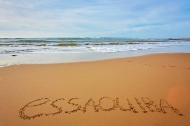 Essaouira şehrinin adı okyanus kıyısındaki kumda yazılıydı. Güzel Atlantik kıyısının arka planına karşı.