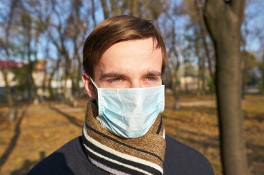 Tıbbi maskeli genç adamın portresi şehir caddesinde duruyor. Dışarıdaki kalabalığın içinde virüsten koruyucu maske takan adam. Coronavirüs salgınından sağIık ve güvenlik kavramı.