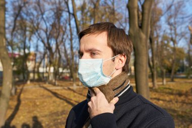 Sokakta yüzüne tıbbi maske takan ceketli bir adam.