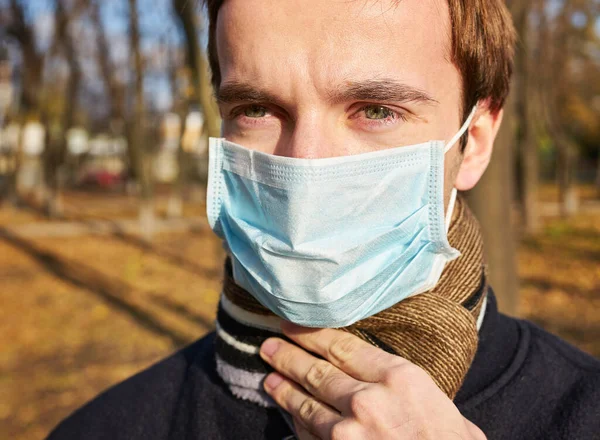 Tıbbi maskeli genç adamın portresi şehir caddesinde duruyor. Dışarıdaki kalabalığın içinde virüsten koruyucu maske takan adam. Coronavirüs salgınından sağIık ve güvenlik kavramı.