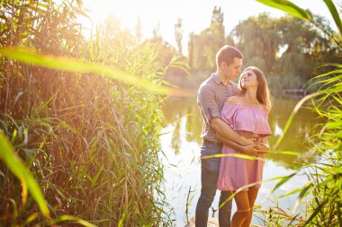 Nehir kenarında durup gün batımını izleyen birbirine aşık bir çiftin bulanık arkaplanı. Renk filtreli fotoğraf.