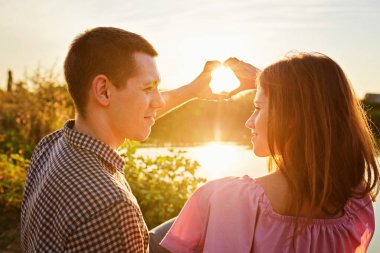 Genç çift göl kıyısında kalp şeklinde ellerini kullanıyor.