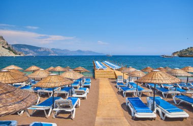 Bulutsuz havada deniz kıyısında akşam kumsalı. Şemsiyeli ve güneşli kumlu bir sahilde gün batımı