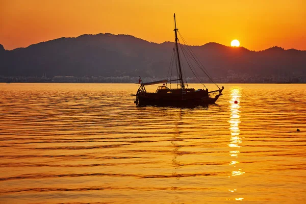 空を背景に黄色い太陽の光で海の中の山と小舟の海辺の夜を眺め夕日 — ストック写真