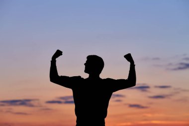 Erkek silueti gün batımında, insan vücudu gökyüzünün doğal renklerinde, elleri havada, neşeli, sağlıklı bir adam doğanın, seyahatin ve özgürlüğün tadını çıkarıyor, başarının kavramsal görüntüsü, büyüme başarısı