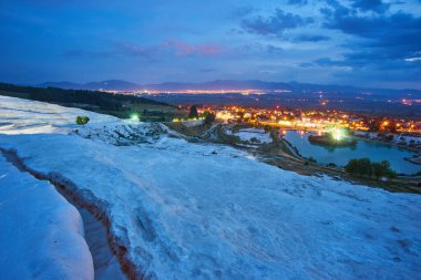 Pamukkale travertines önde. Günbatımı gökyüzü ve arka planda aydınlık evler.