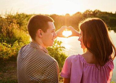 Genç çift göl kıyısında kalp şeklinde ellerini kullanıyor.