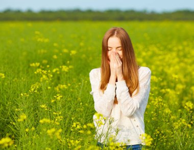 Polene ve çiçek açma mevsimine alerjisi olan kızıl saçlı bir kız çiçek tarlasında hapşırıyor.