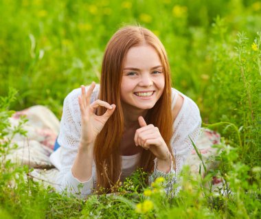 Güzel kızıl saçlı kadın, güzel bir yaz gününde parkta çimlerin üzerinde uzanıyor.