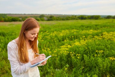 Dışarıdaki çimlerin üzerine kalem yazan kızıl saçlı kız.
