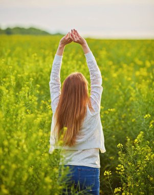 Güneşli bir günde kolza tohumu tarlasında kızıl saçlı kız.