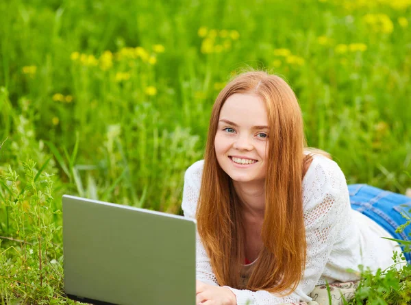 girl working in nature with a laptop lying on the green grass. The girl works as a freelance traveler. Freelancer with a laptop in nature