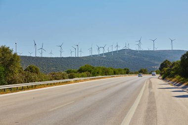 Rüzgar türbini yeşil ve sarı alanda. Önde boş bir yol, arkasında bulutlar olan mavi bir gökyüzü. Alternatif enerji kaynağı, üretim ve güç üretimi. Ekoloji ve özgürlük kavramı.