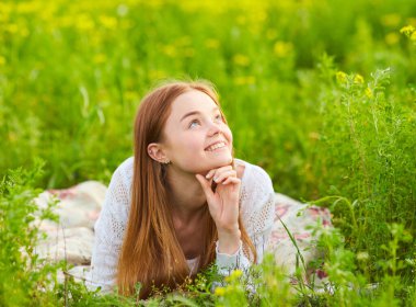 Güzel kızıl saçlı kadın, güzel bir yaz gününde parkta çimlerin üzerinde uzanıyor.