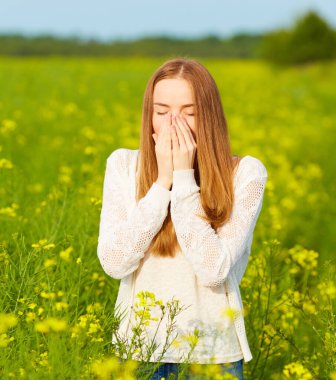 Polene ve çiçek açma mevsimine alerjisi olan kızıl saçlı bir kız çiçek tarlasında hapşırıyor.