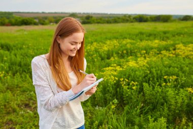 Dışarıdaki çimlerin üzerine kalem yazan kızıl saçlı kız.