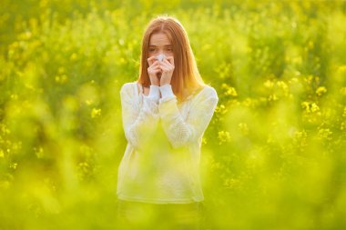 Polene ve çiçek açma mevsimine alerjisi olan kızıl saçlı bir kız çiçek tarlasında hapşırıyor.