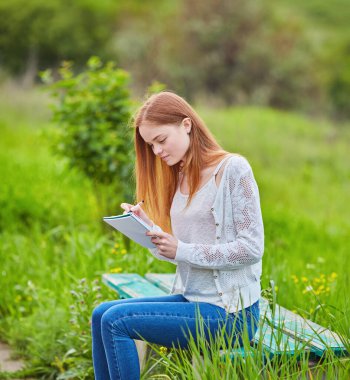 Dışarıdaki çimlerin üzerine kalem yazan kızıl saçlı kız.