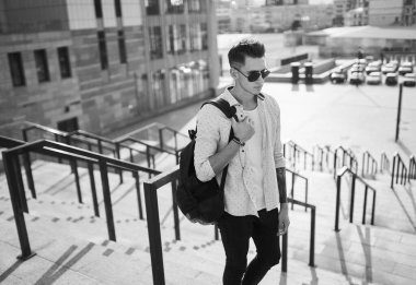 Güneş gözlüklü genç adam merdivenlerden siyah bir sırt çantasıyla çıktı.