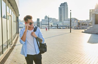 Elinde güneş gözlüğü olan siyah bir sırt çantalı genç bir adam..