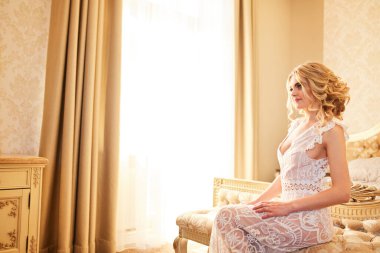 Genç ve güzel bir gelinin şehvetli sabah hazırlığı. Düğün için. Gelinin harcı evin iç kısımlarında. Peignoir 'deki seksi hassas gelin. Lüks saçlı ve makyajlı gelin..