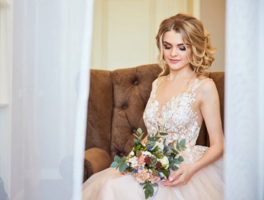 Genç ve güzel gelin bir sandalyede oturuyor ve gülümsüyor.