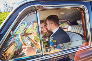 Zarif bir gelin gülümsüyor ve yakışıklı bir damat onu arabada öpüyor. Geçmişe dönük alışılmadık lüks bir düğün çifti. romantik an