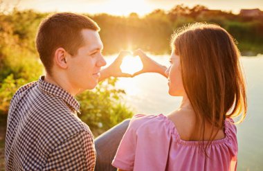 Genç çift göl kıyısında kalp şeklinde ellerini kullanıyor.