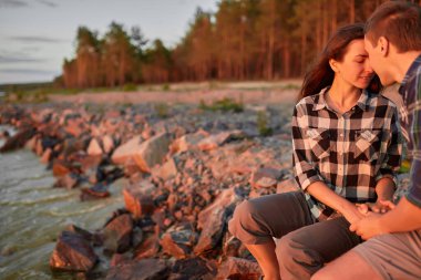 Sevgi dolu bir çift gün batımında kumlu kumsalda eğleniyor ve sarılıyor. Birbirlerine bakıyor ve mutlu bir şekilde gülümsüyorlar..