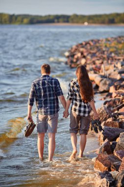 Gün batımında sahilde yürüyen bir çift.