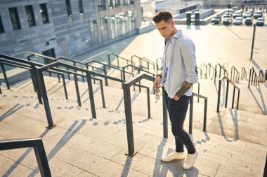 Elinde güneş gözlüğü olan siyah bir sırt çantalı genç bir adam..