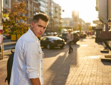 Sırt çantalı genç Avrupalı bir adam şehir caddesinde duruyor.