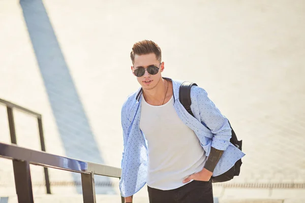Young man in sunglasses walks up the stairs with a black backpack