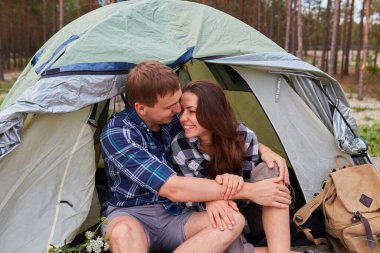 Dışarıda kamp yapan ve çadırda oturan romantik bir çift. Mutlu adam ve kadın romantik bir kamp tatilindeler..