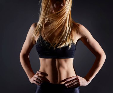 Spor salonunun siyah duvarında duran sarışın kız. Vücut geliştirme ve saç süpürme