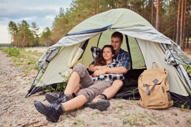 Dışarıda kamp yapan ve çadırda oturan romantik bir çift. Mutlu adam ve kadın romantik bir kamp tatilindeler..
