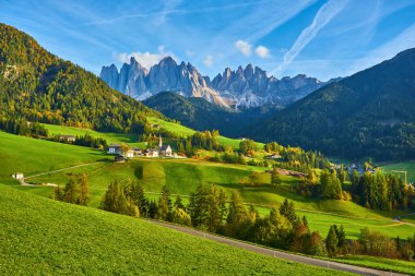 Santa Maddalena köyünde muhteşem bir sonbahar manzarası var. Kilise, renkli ağaçlar ve yükselen güneş ışınları altında çayırlar. Dolomite Alpleri, Güney Tyrol, İtalya.