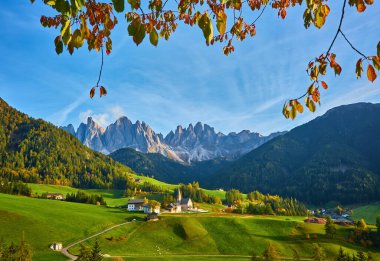 Santa Maddalena köyünde muhteşem bir sonbahar manzarası var. Kilise, renkli ağaçlar ve yükselen güneş ışınları altında çayırlar. Dolomite Alpleri, Güney Tyrol, İtalya.