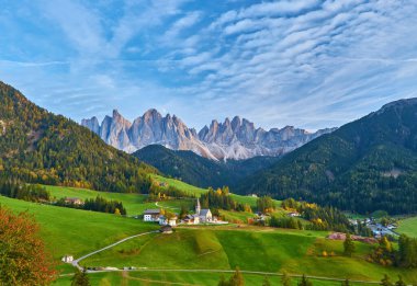 Santa Maddalena köyünde muhteşem bir sonbahar manzarası var. Kilise, renkli ağaçlar ve yükselen güneş ışınları altında çayırlar. Dolomite Alpleri, Güney Tyrol, İtalya.