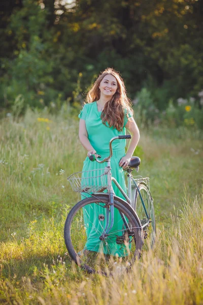 Beautiful young woman with an old bicycle in the field — Stock Photo, Image