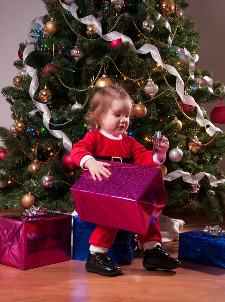 Cute Baby Girl w kostium Santa otwarcia obecny w pobliżu Christm — Zdjęcie stockowe