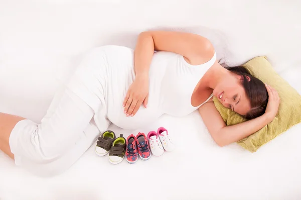 Small shoes for the unborn baby opposite the belly of pregnant w — Stock Photo, Image
