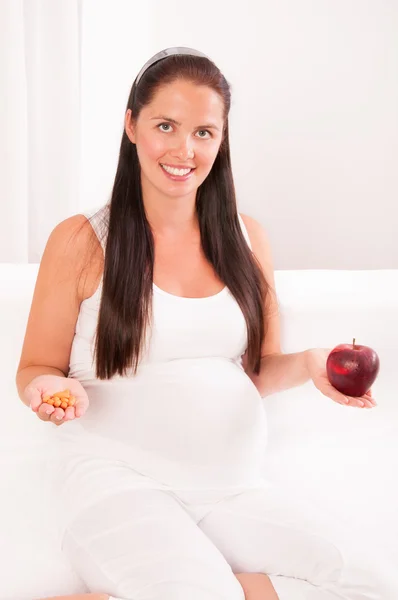 Hermosa mujer embarazada con una manzana en una mano y vitaminas — Foto de Stock