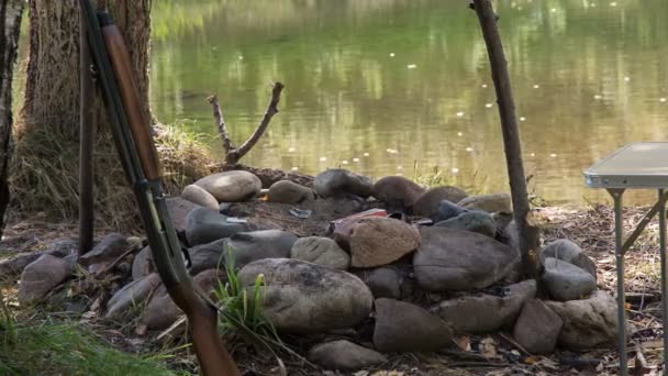 La escopeta se encuentra en el fuego extinto en la orilla del río — Vídeos de Stock